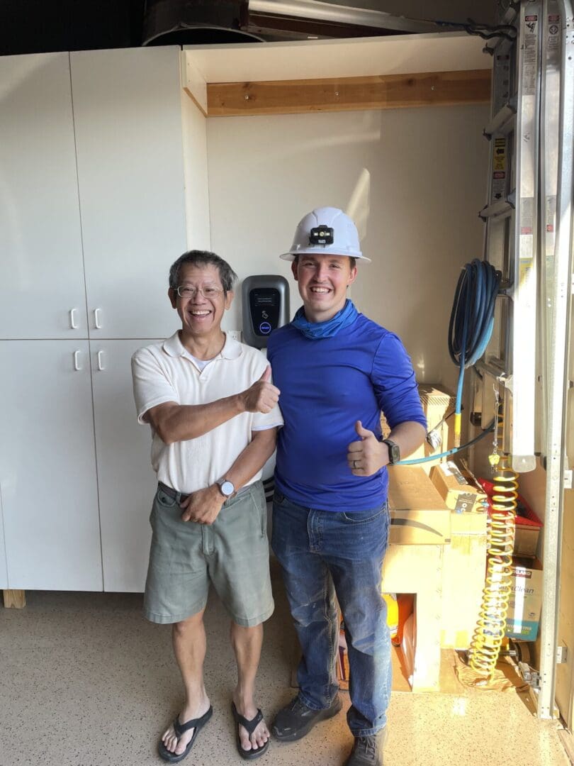 Two men in a garage, one giving thumbs up.